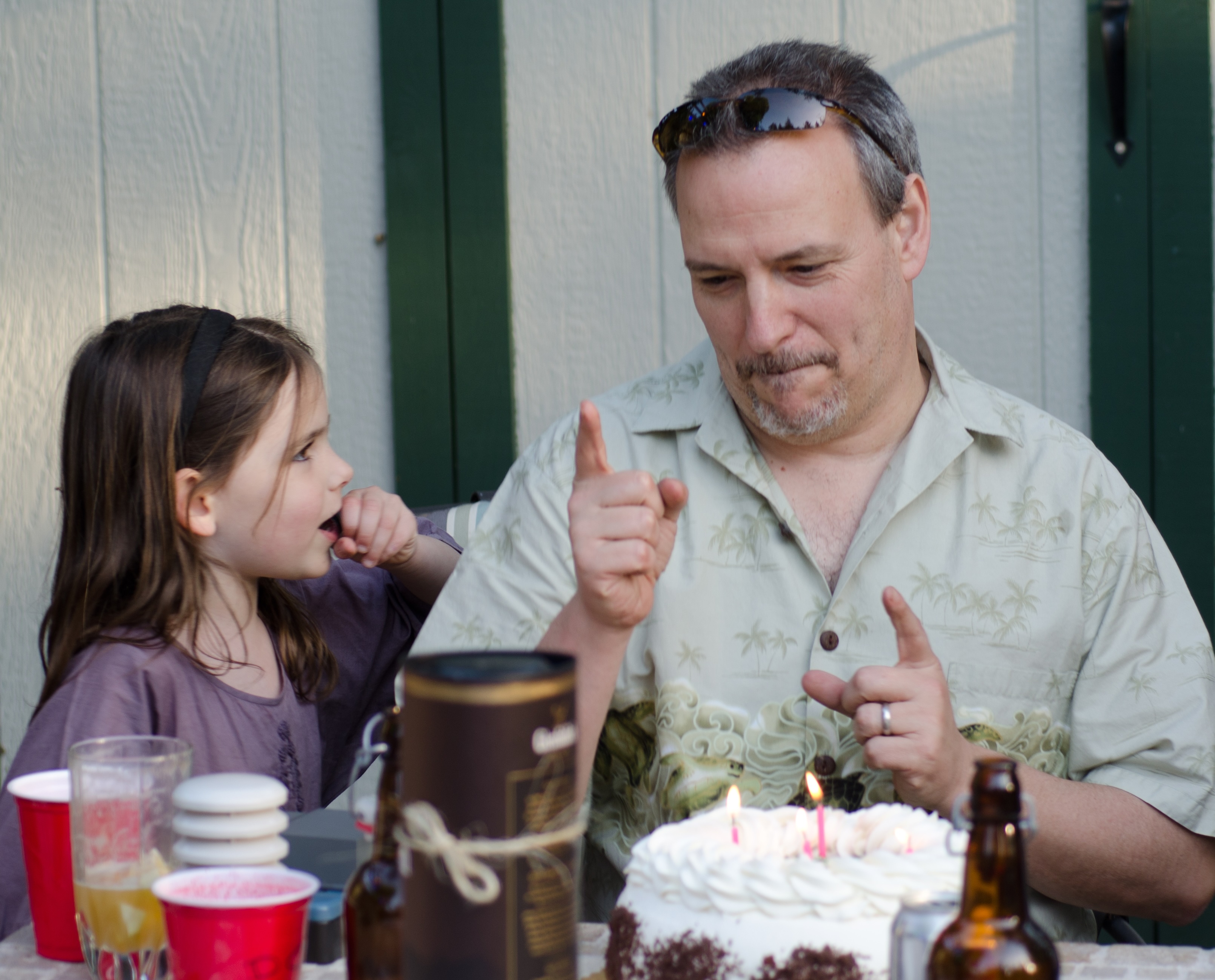 A man sitting at a table with a birthday cake in front of him. A girl on the left looking at the man.